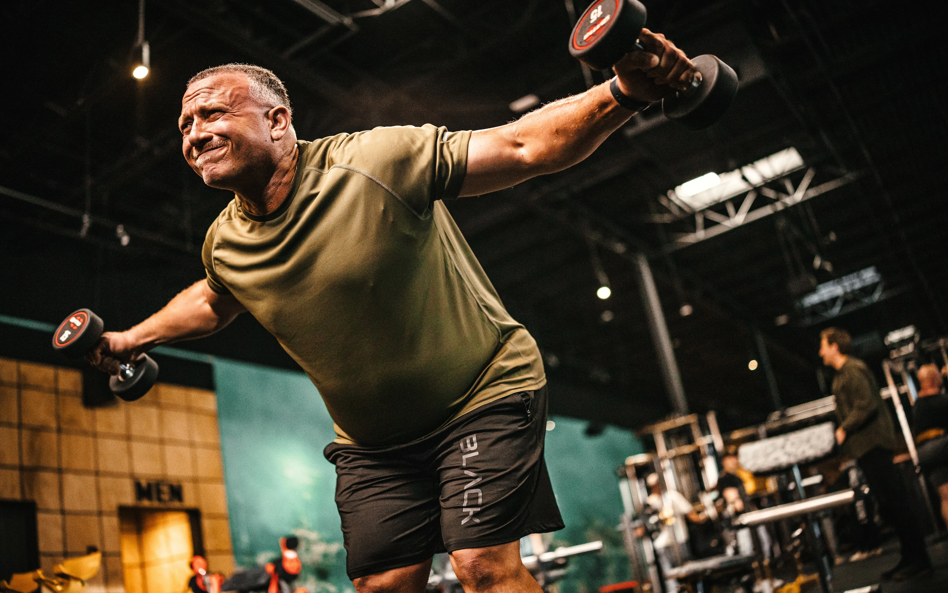 Man performing dumbbell lateral raises for a delt workout.
