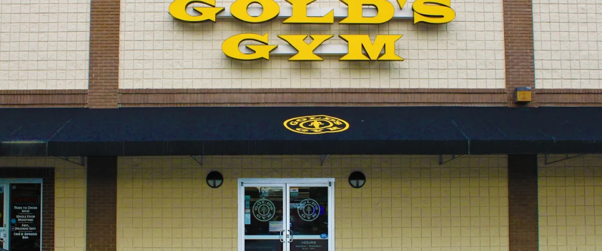 Exterior of Gold’s Gym Charleston with yellow logo above a black awning and glass entry doors.