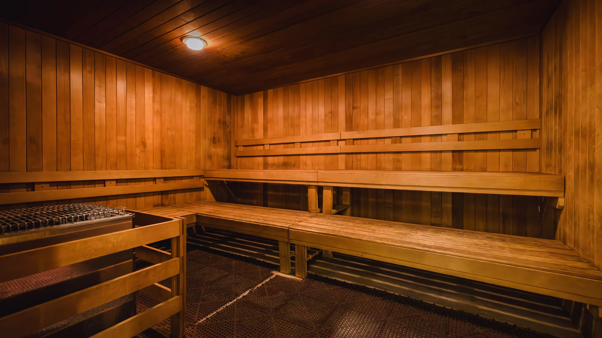 Dimly lit sauna room at Gold's Gym Austin (Anderson Arbor) with warm wood-paneled walls, matching wooden benches, and a dark, textured floor surrounding a corner heating element.