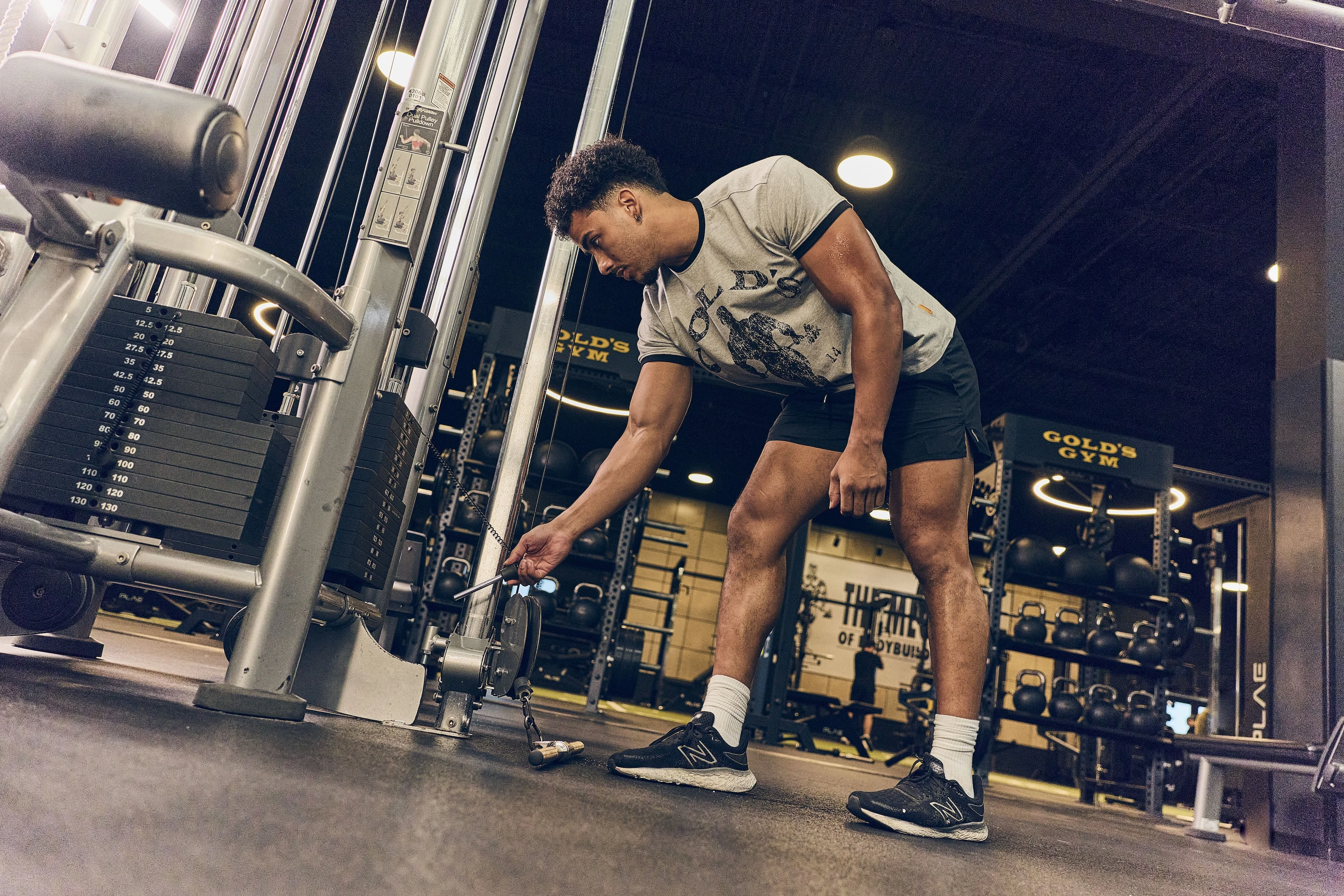 Gold’s Gym member adjusting a cable machine before starting a strength training workout.