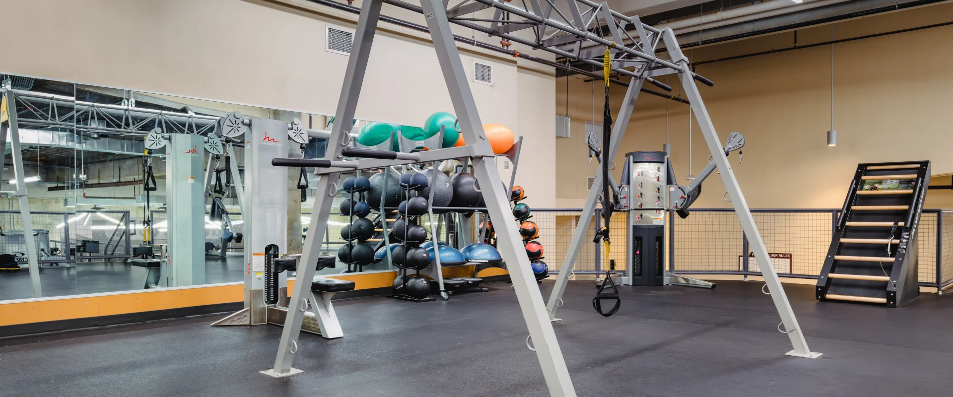 Functional training area at Gold's Gym Austin (Downtown) featuring a TRX training frame, a rack of medicine balls, resistance bands, cable machines, and a stair climber, with large mirrors reflecting the space.