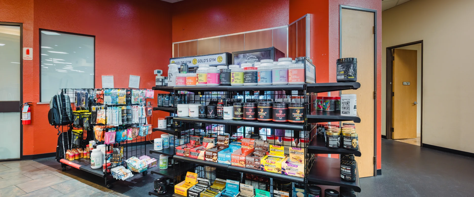 Pro Shop stocked with protein powders, supplements, and energy bars. Bright lighting creates an energetic atmosphere.