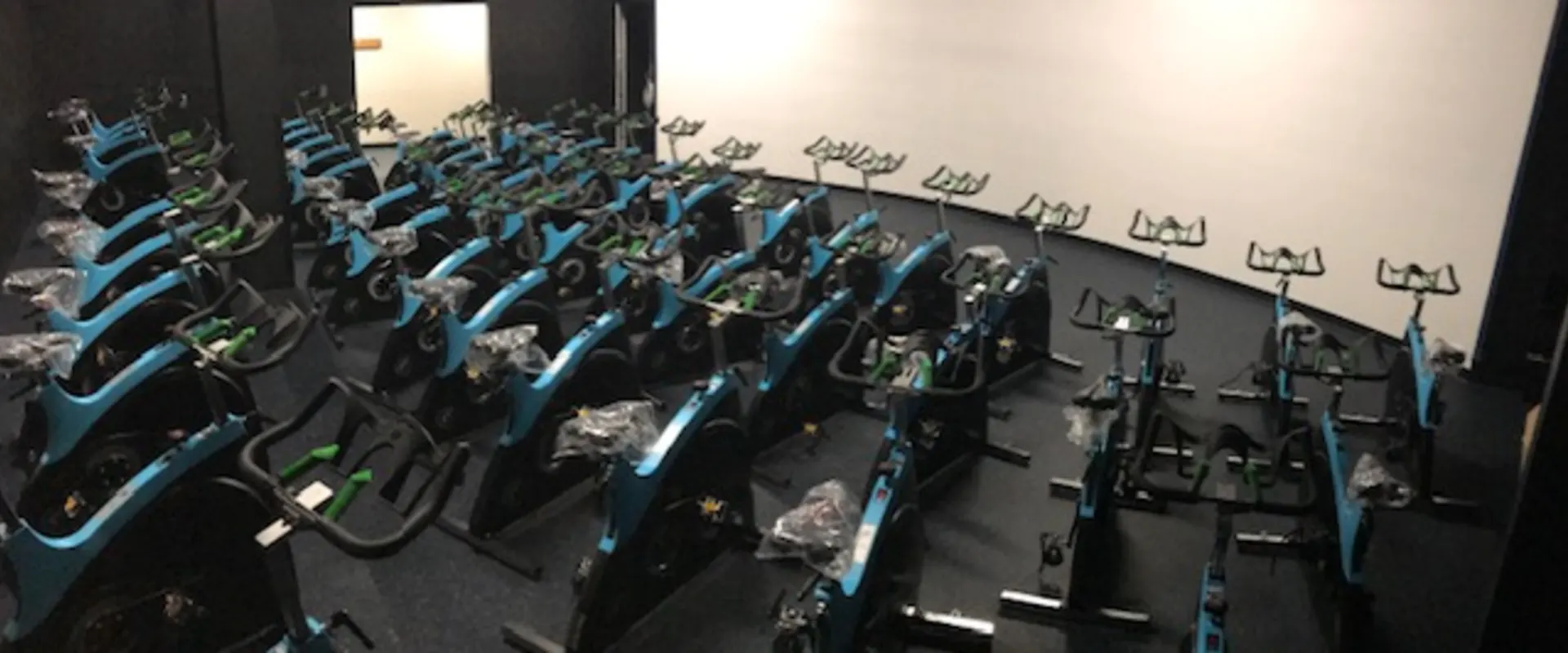 A large room filled with numerous stationary exercise bikes arranged in rows, with a white wall in the background.