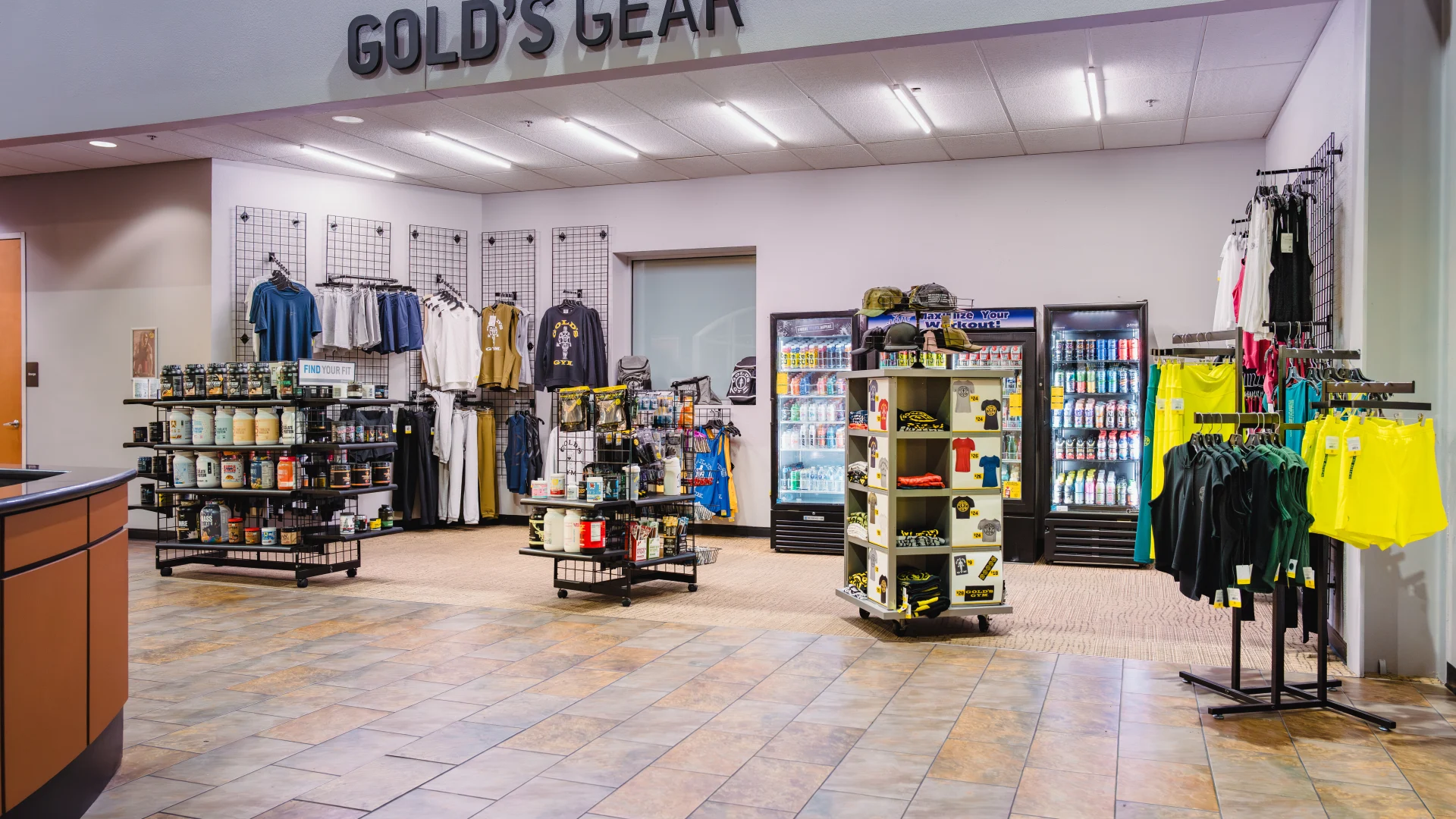 Pro shop at Gold's Gym Waco featuring a variety of fitness merchandise, including supplements, apparel, and accessories displayed on shelves and racks. Refrigerated coolers stock drinks and protein snacks, while tile flooring and bright lighting enhance the retail space.