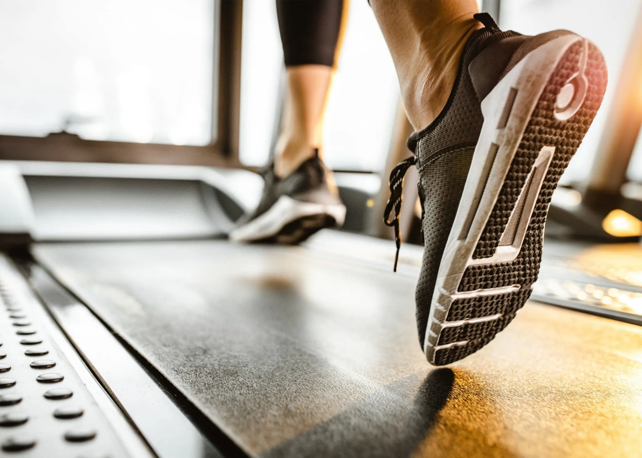 The image shows a close-up view of a person's feet wearing athletic shoes on a treadmill in a fitness center or gym.
