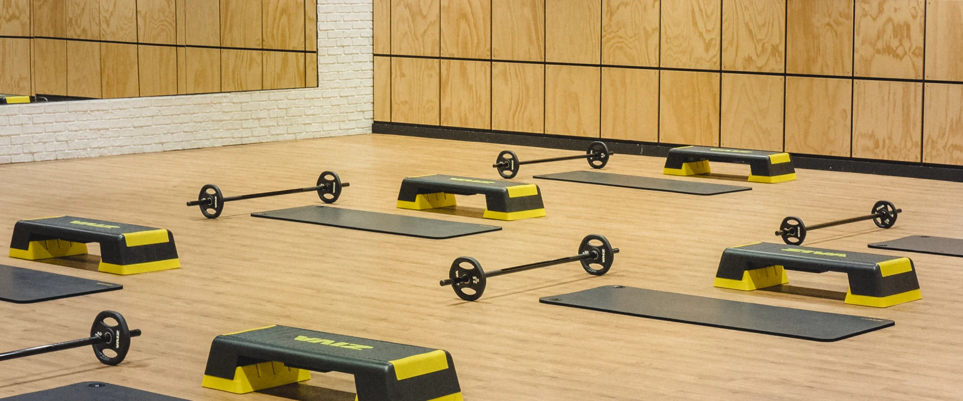Step platforms, barbell weights, and exercise mats arranged in a group exercise studio at Gold’s Gym Flower Mound, featuring mirrored and wooden panel walls.