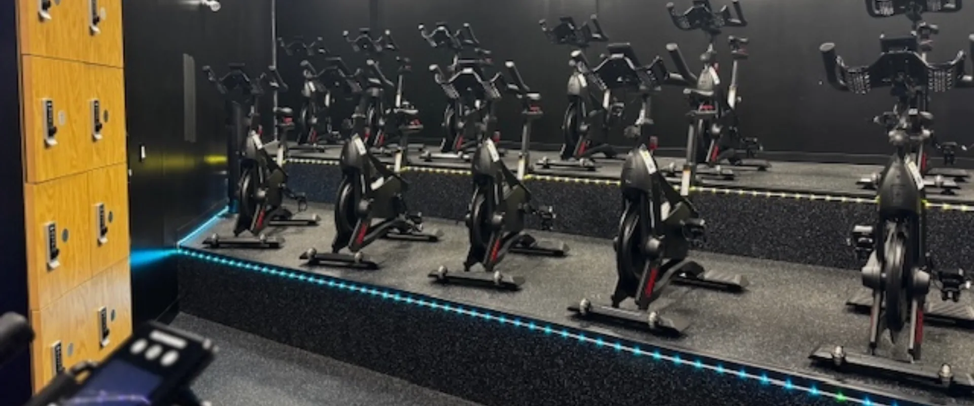 Spacious spin studio with multiple stationary bikes and dark walls.