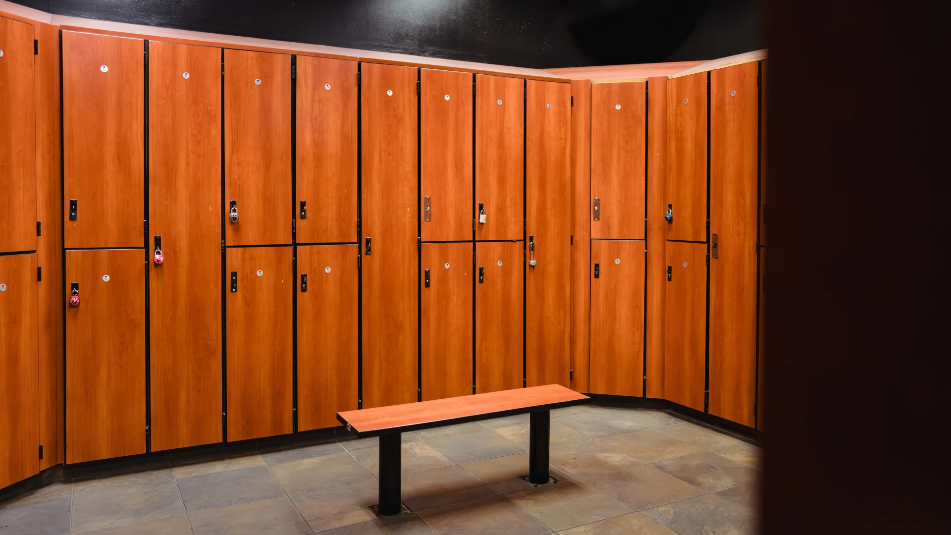 Empty locker room with wooden lockers and a bench on a tiled floor.