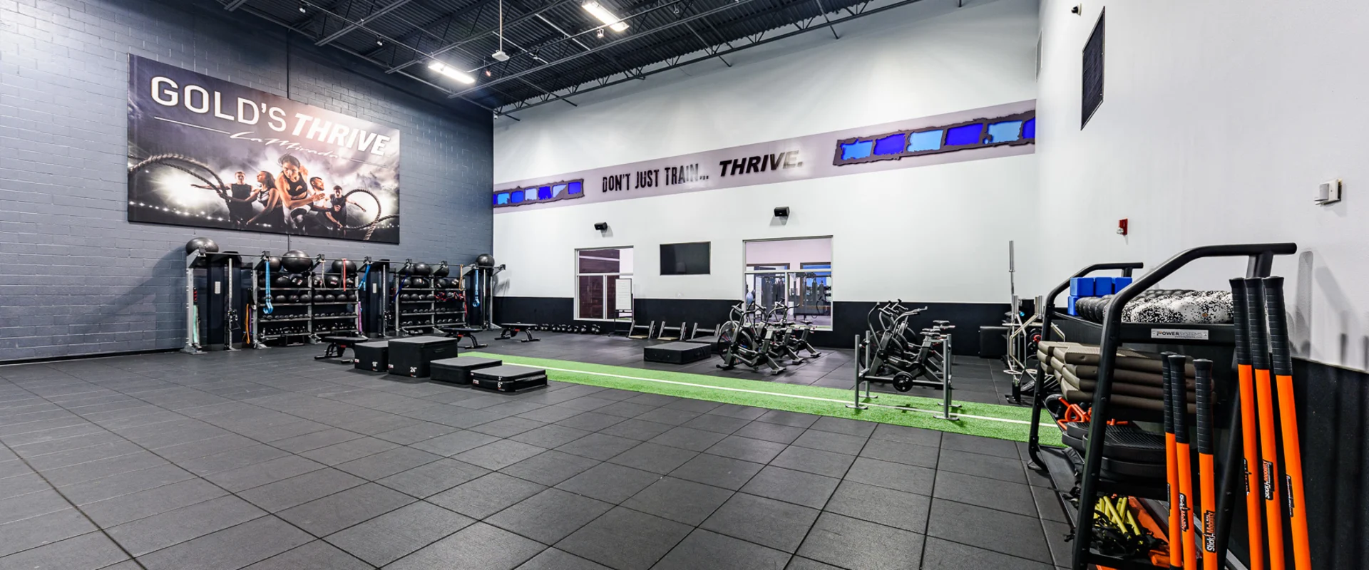 A spacious functional training zone equipped with battle ropes, plyometric boxes and medicine balls. A turf strip runs through the area, and storage racks keep various training tools organized.