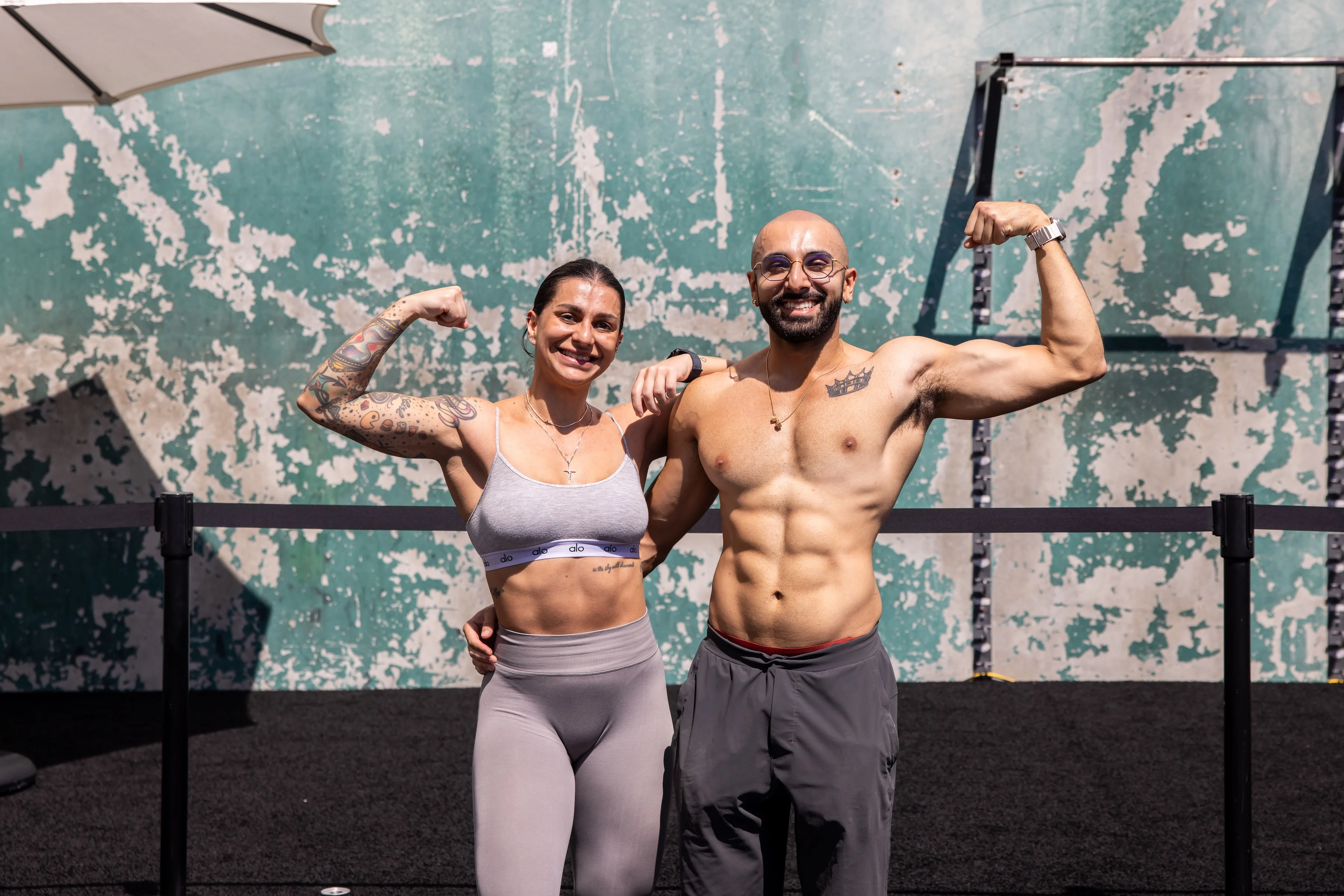 Man and woman flexing their biceps together outdoors after a workout at Gold's Gym