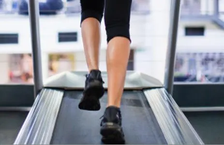 The image shows a person's legs and feet on a treadmill, with a blurred background of what appears to be a fitness center or gym.