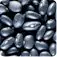 The image depicts a close-up view of a collection of smooth, dark-colored stones or pebbles, creating a textured and abstract visual pattern.