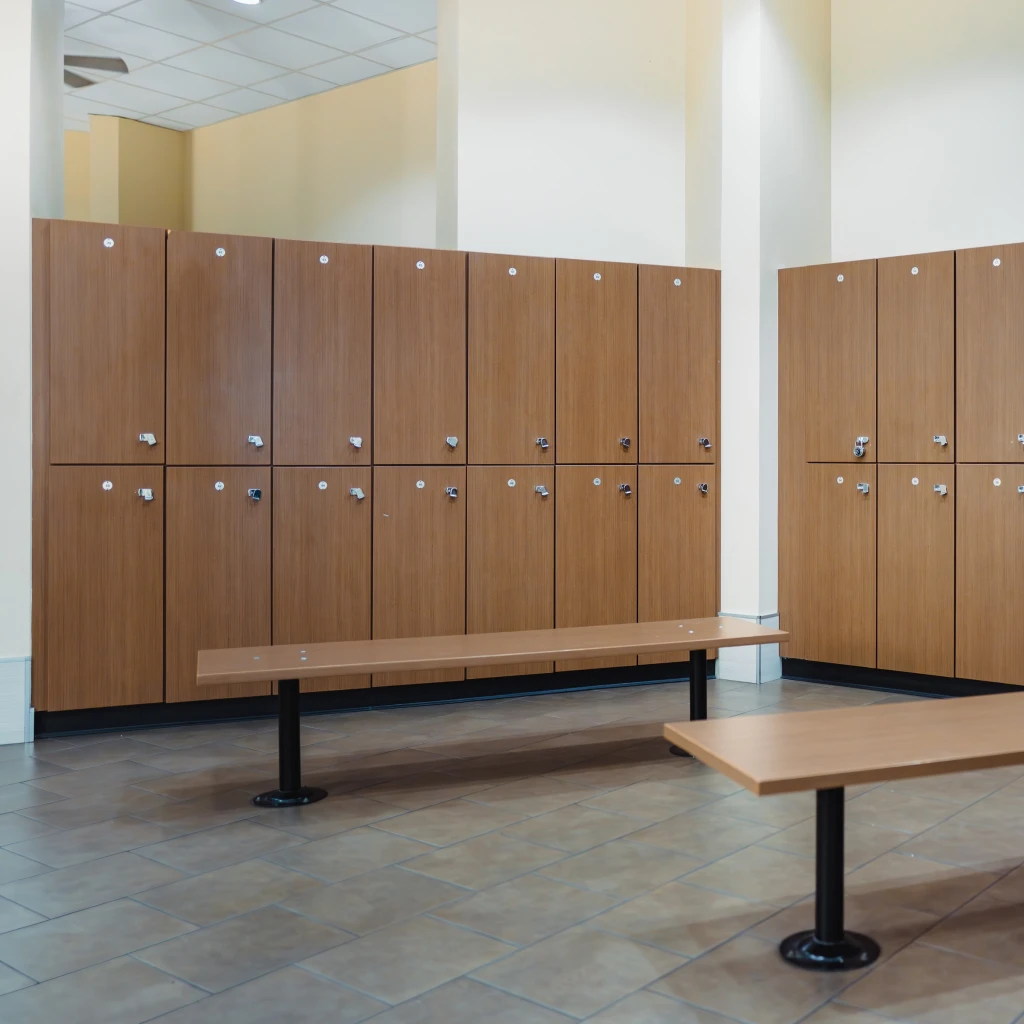 Wooden locker room with tan benches and brown lockers on tiled floor. The setting is clean, orderly, and brightly lit, conveying a calm mood.