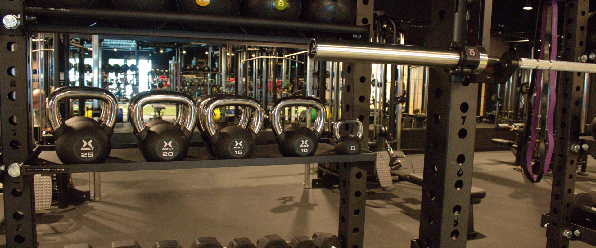 Functional training area at Gold's Gym Austin, Burnet Rd with a neatly organized rack of kettlebells, dumbbells, medicine balls, and resistance bands, all set against mirrored walls and strength equipment.