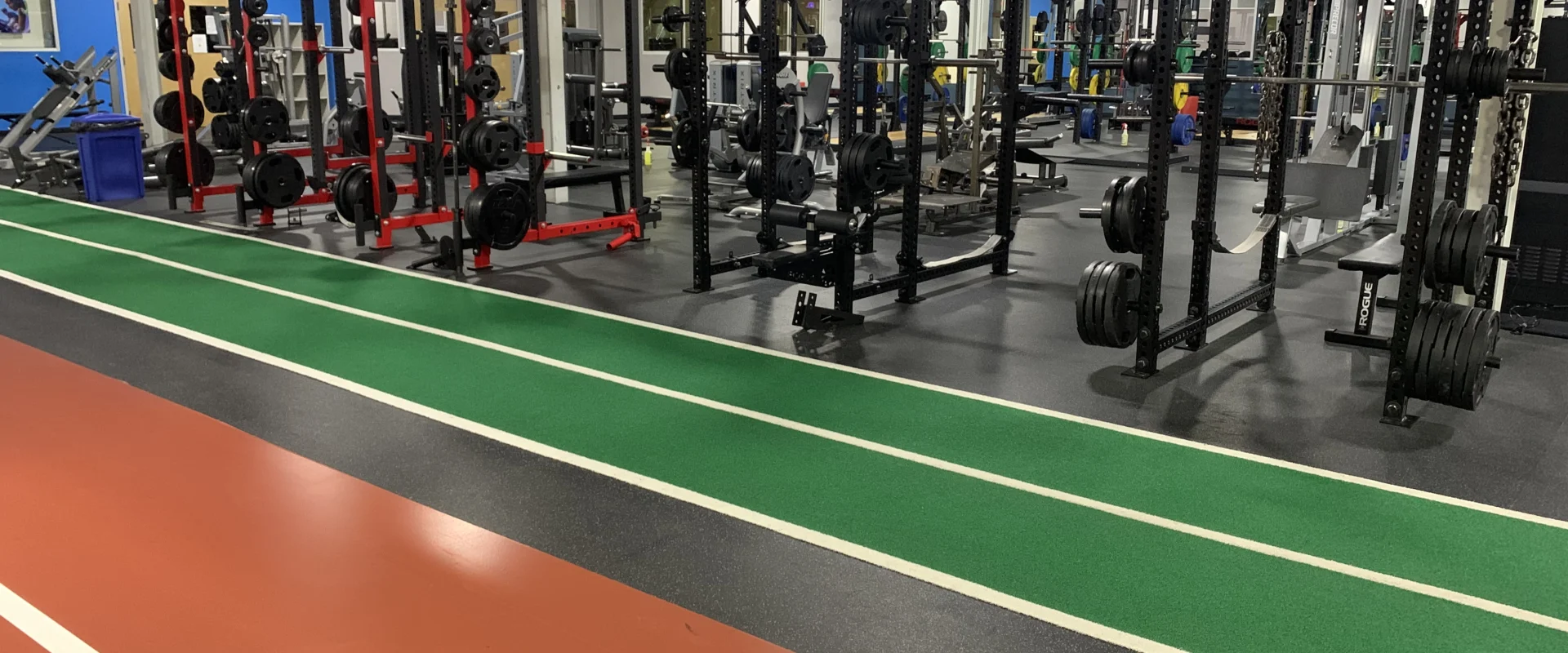 A large, well-equipped gym with various exercise equipment and machines, including weight racks, benches, and cardio machines, set against a backdrop of colorful walls and flooring.