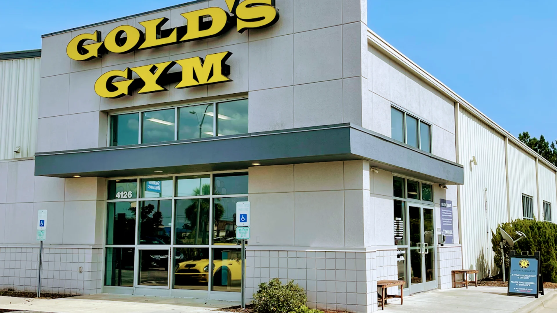 Exterior of Gold’s Gym Jacksonville with yellow signage and glass entrance in a light gray building.