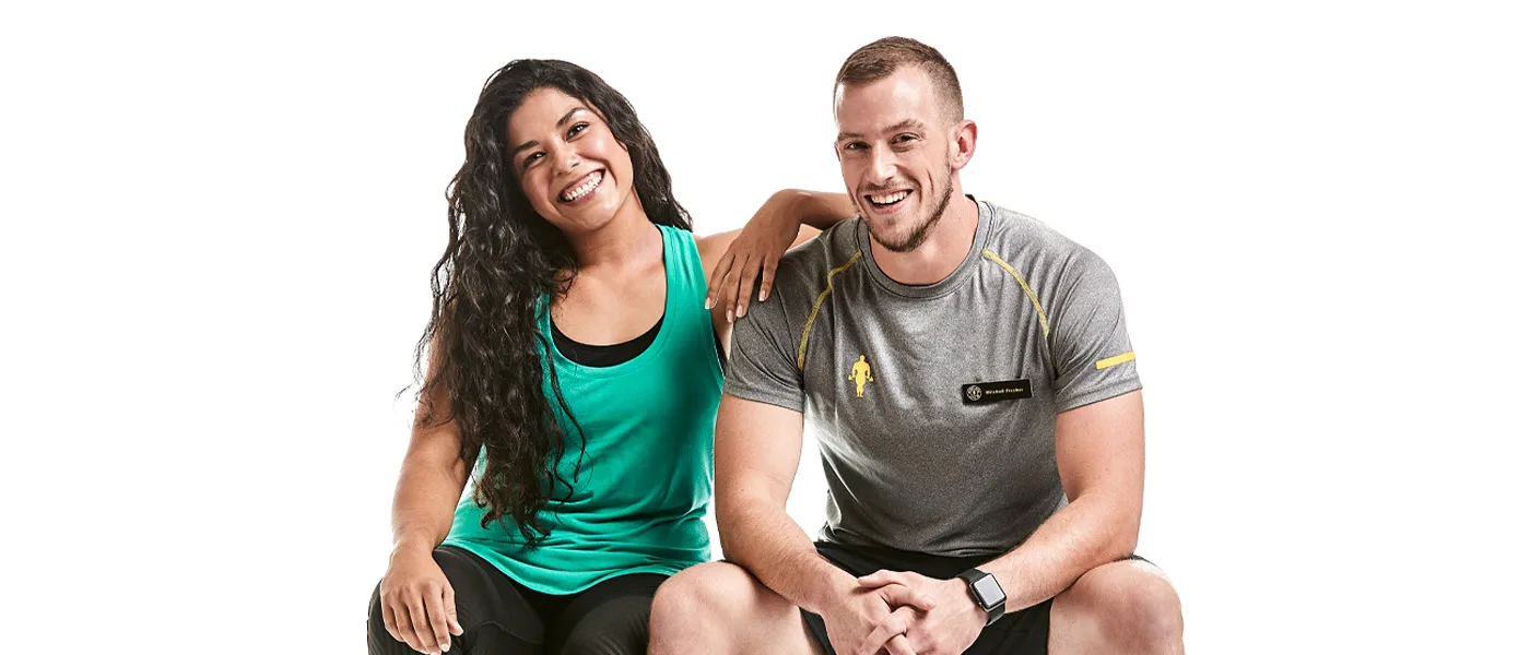 Two young people, a woman in a green top and a man in a gray shirt, are sitting together and smiling happily.