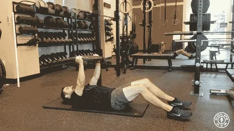 A person is lying on a fitness mat in a gym setting, surrounded by various exercise equipment and storage shelves.