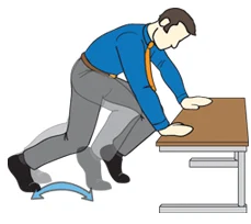 A person in a blue shirt and gray pants is leaning over a desk, appearing to be working on something.