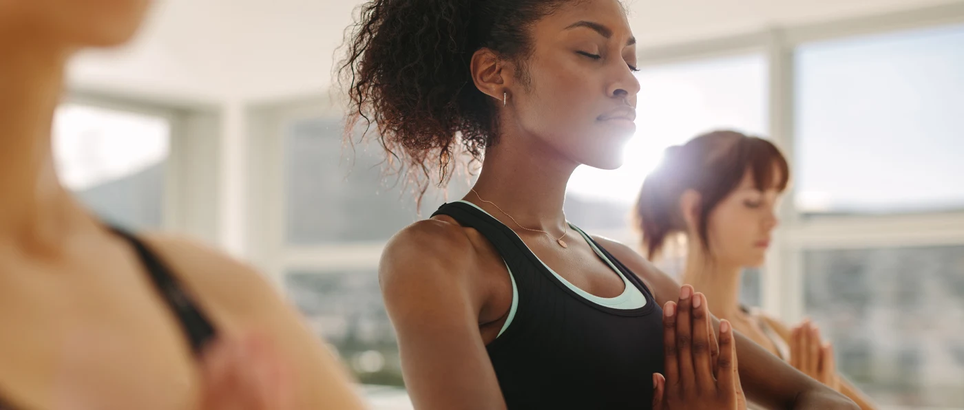The image shows a woman with curly hair practicing yoga or meditation, with another person in the background.