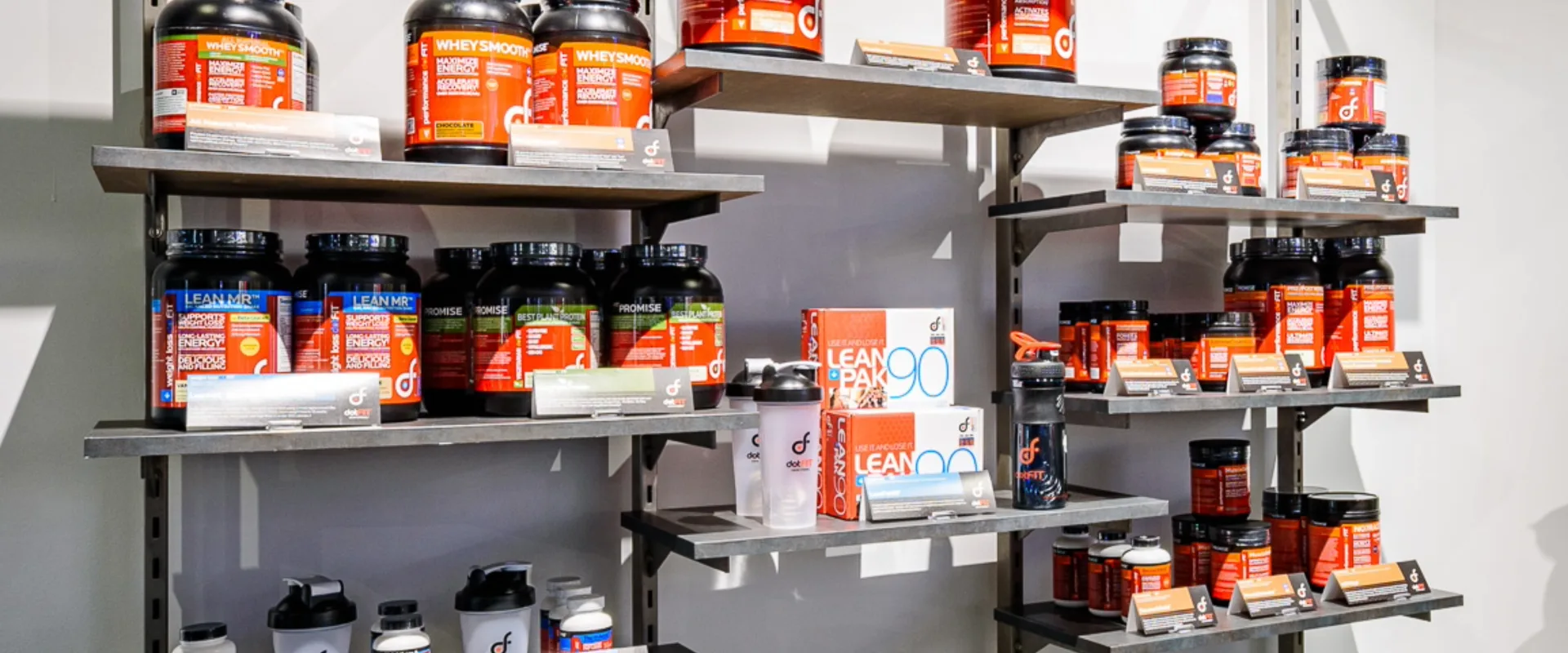 Supplement display at Gold’s Gym Thousand Oaks, featuring a variety of protein powders, vitamins, and nutrition bars. Shelves are stocked with large and small containers of protein, pre-workout, and recovery supplements. Shaker bottles and meal replacement products are also available. The display is organized with labeled sections for easy selection.