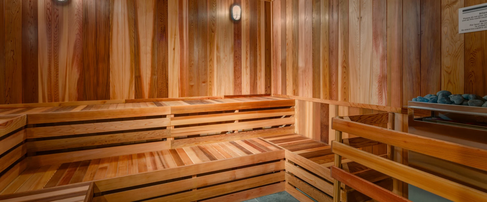 A cozy and warm-toned wooden sauna interior with benches, shelves, and lighting fixtures, creating a serene and relaxing atmosphere.