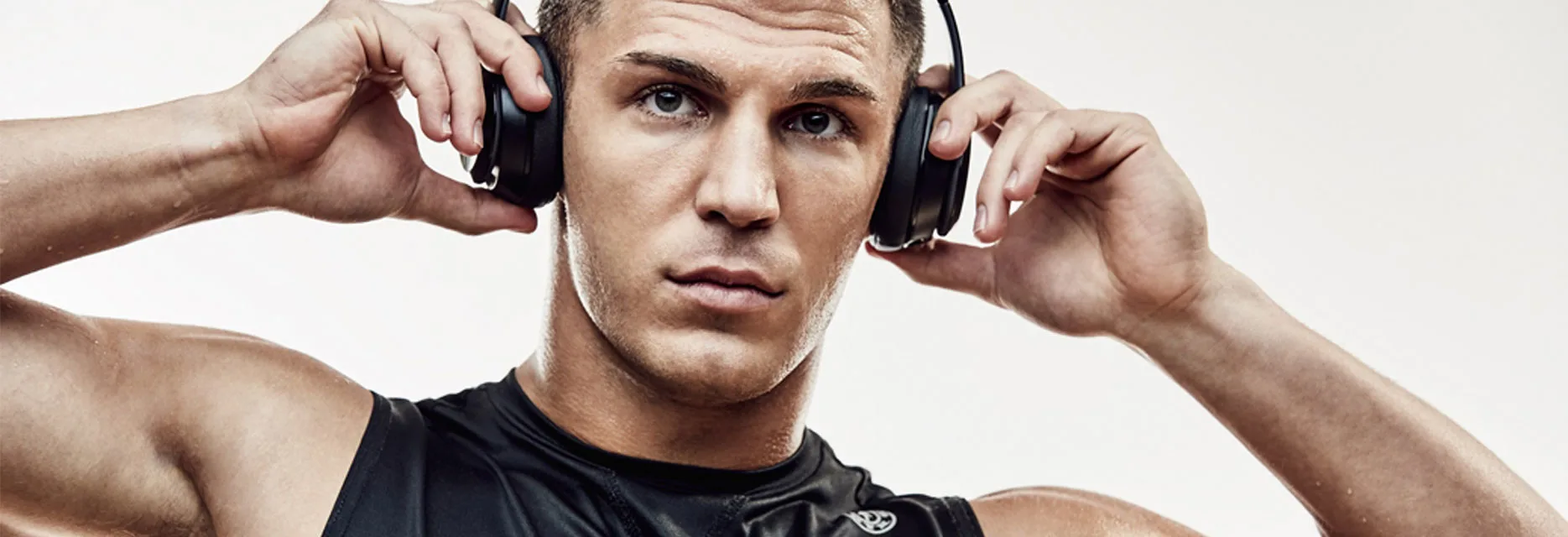 A close-up portrait of a young man wearing headphones, with a serious expression on his face, set against a plain white background.