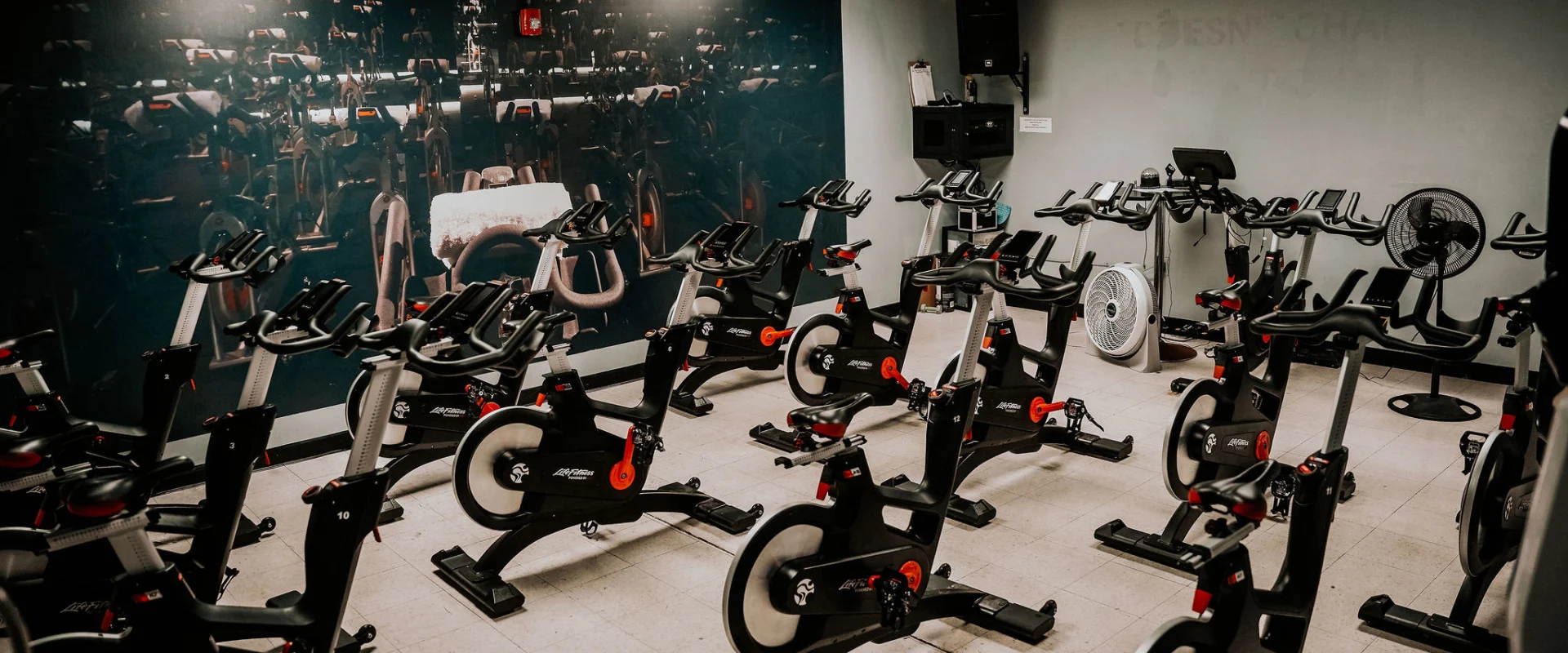 Group cycle studio at Gold's Gym Smyrna, Tennessee, featuring rows of stationary bikes arranged in a room with a large photo of bikes on the wall. A sound system and fans are visible in the background.