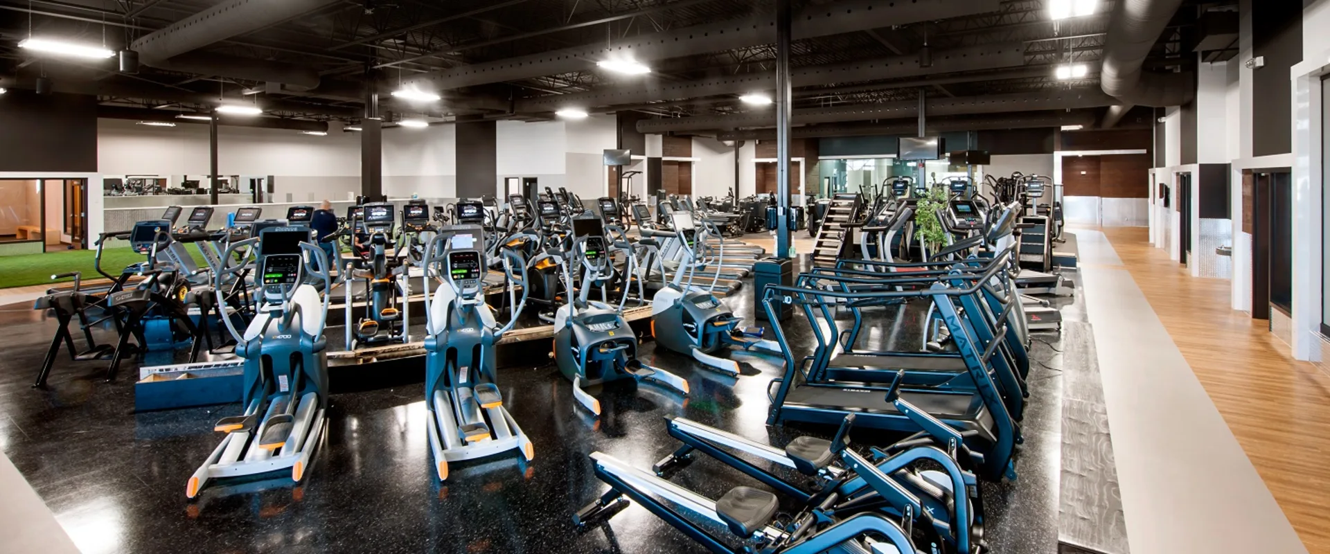 Cardio equipment section at Gold’s Gym Laval, showing neatly arranged treadmills, stair climbers, and ellipticals on glossy black flooring. Industrial lighting and exposed ceilings give the space a modern, open feel.