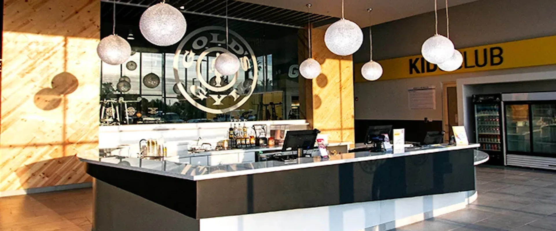 Interior of Gold’s Gym Edinburg with modern front desk, hanging lights, and Gold’s Gym logo on glass wall.