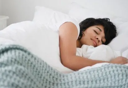 A young woman is sleeping peacefully on a bed, wrapped in a cozy, patterned blanket.
