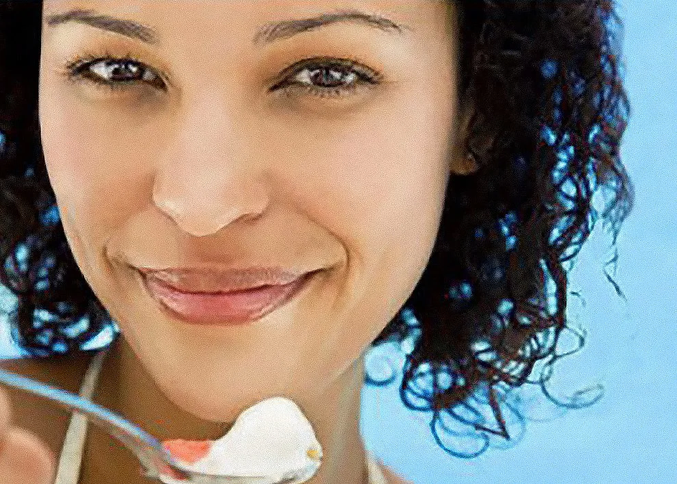 A smiling woman with curly dark hair against a blurred blue background.