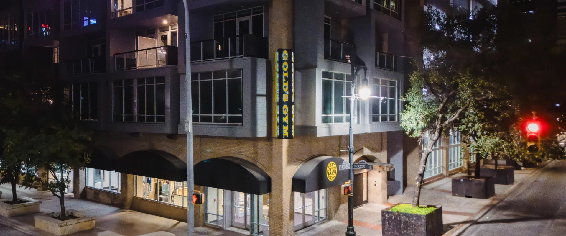 Exterior of Gold's Gym Austin (Downtown) at night time, featuring a modern building design with large windows and a prominent Gold's Gym sign on the facade.