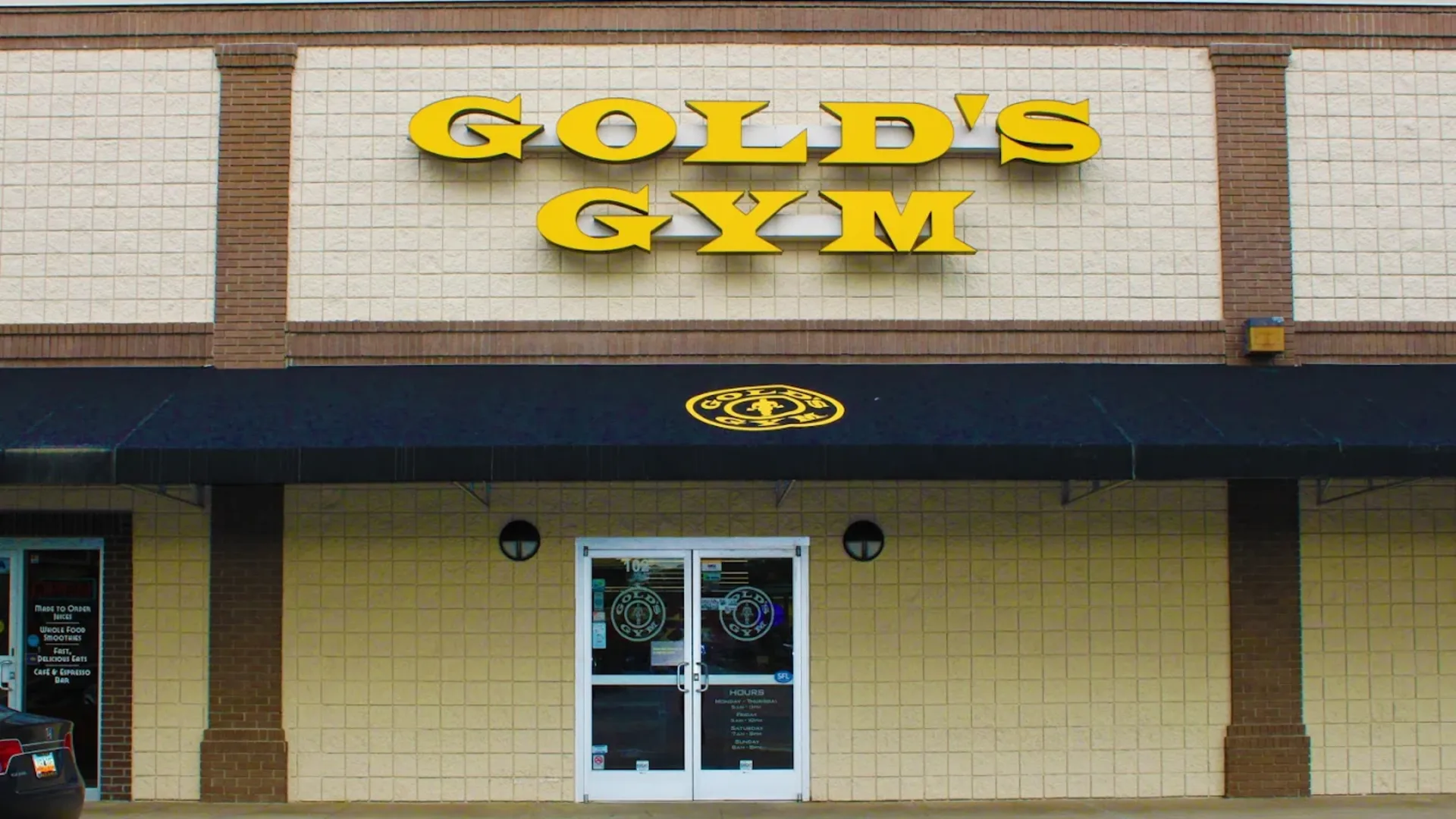 Exterior of Gold’s Gym Charleston with yellow logo above a black awning and glass entry doors.