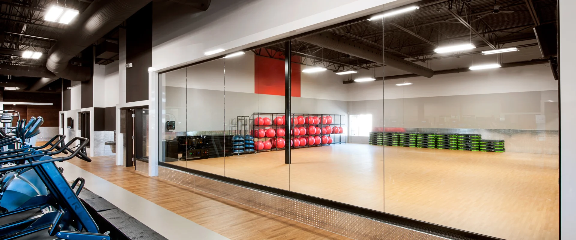 Spacious GGX group fitness studio at Gold’s Gym Laval with floor-to-ceiling mirrors, wood flooring, red exercise balls, stacked steps, and ample natural light.