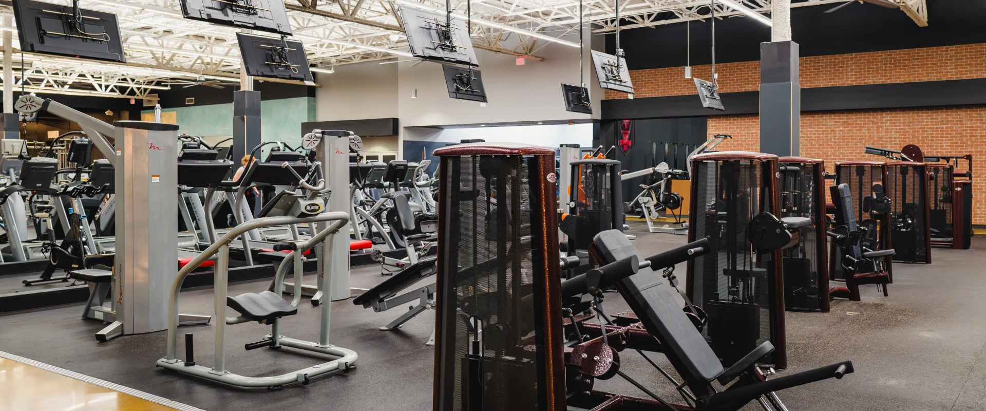 Gold's Gym machine weight area featuring various strength-training equipment and cardio machines, with a bright, open space and mounted TVs above.