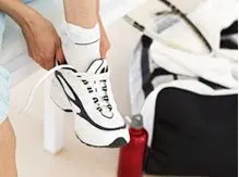 A person's legs and feet wearing white sneakers with a black and white design, standing on a tiled floor with a black and white pattern.