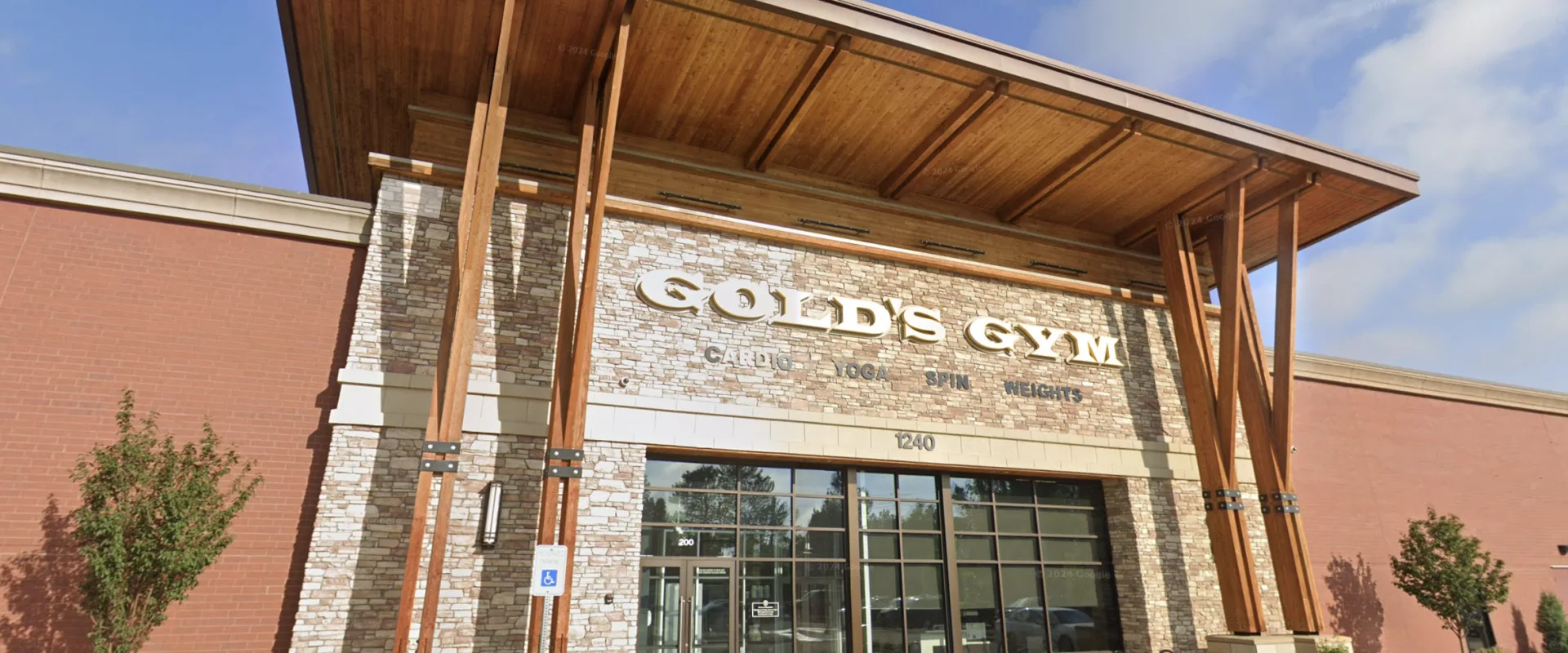 Exterior of Gold’s Gym Longmont with wood beams, stone facade, and glass entrance on a sunny day.