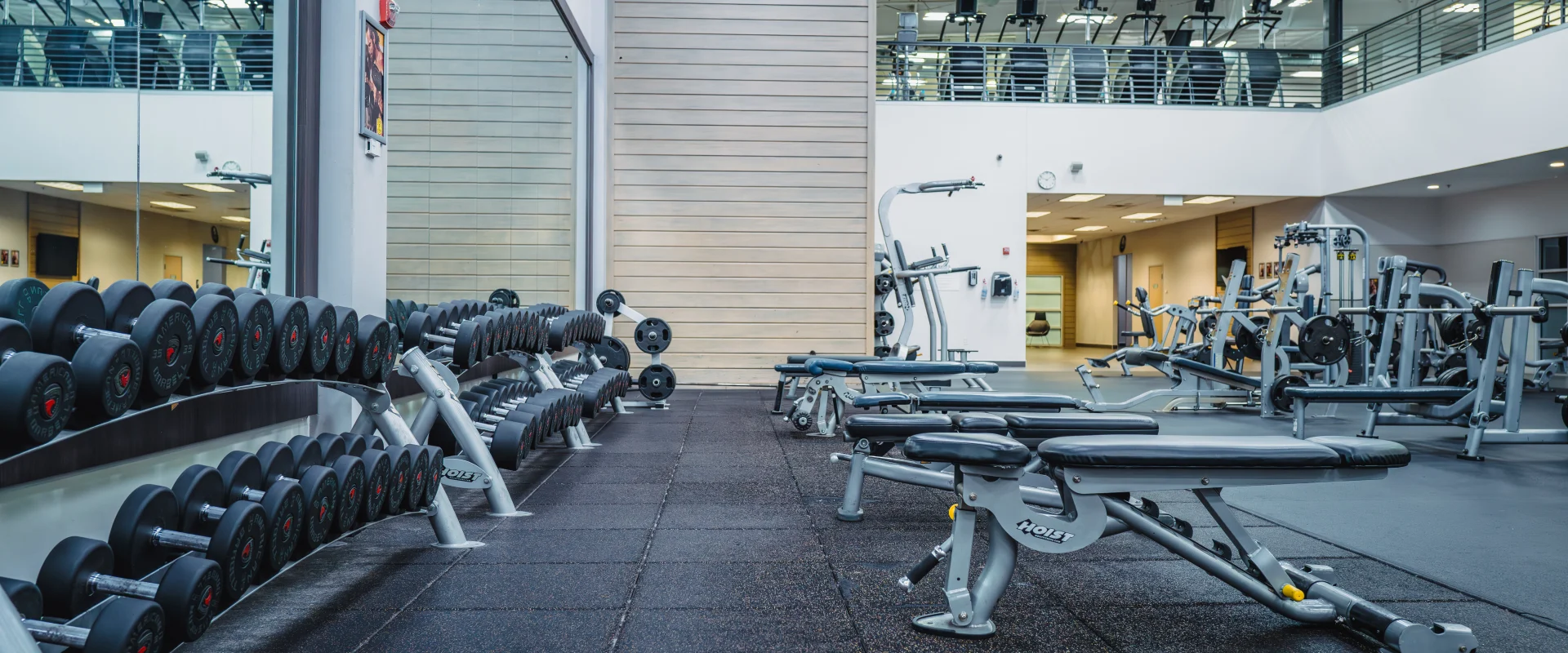 Dumbbell area at Gold's Gym Oklahoma City (Moore) featuring mirrored walls, racks of neatly arranged dumbbells, adjustable weight benches, and a view of additional workout equipment.