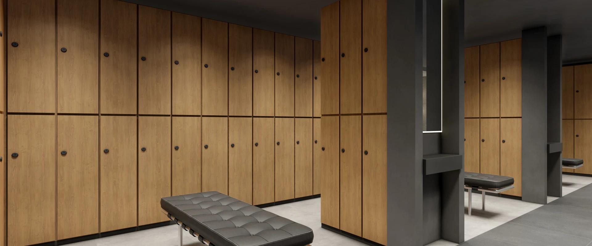 Rendering of the locker room at Gold’s Gym Los Angeles (Beverly Center), featuring rows of wood-finished lockers with black handles lining the walls. A black cushioned bench with a metal frame sits in the center of the space. Built-in grooming stations with illuminated mirrors and dark countertops are positioned between locker sections. The flooring consists of large-format tiles in contrasting light and dark tones. This digital rendering previews the planned design for the upcoming location.