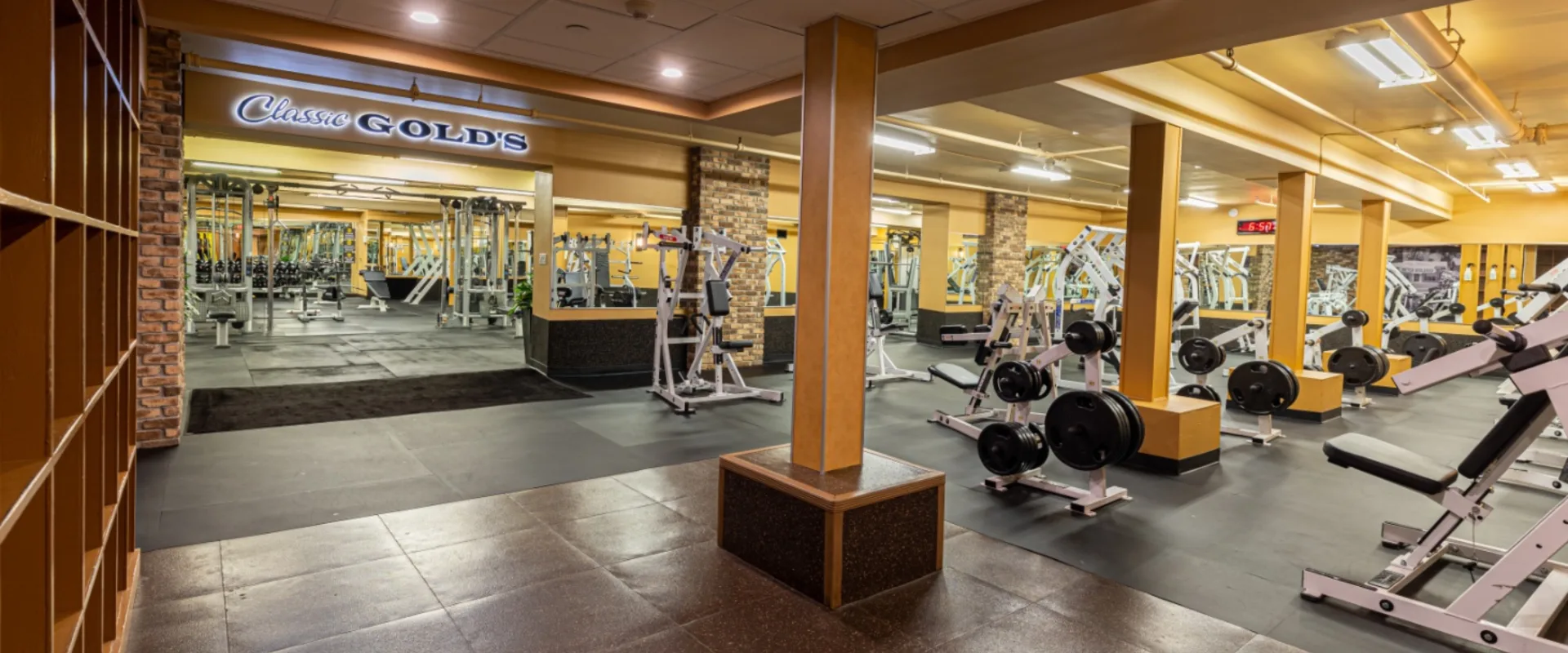 Free weights area at Gold’s Gym New York (East Northport), located in the “Classic Gold’s” section, featuring plate-loaded machines, weight racks, and benches. The space includes mirrored walls, brick accents, and wide walkways for easy movement. Rubber flooring provides a solid foundation for heavy lifting, while overhead lighting brightens the strength-focused environment.