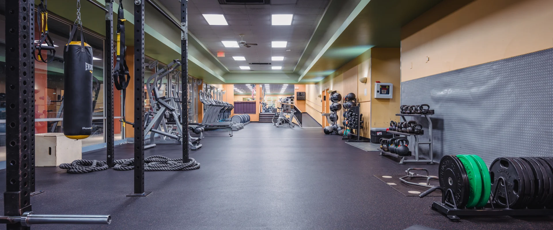 A spacious, well-lit gym with exercise equipment. Features include a punching bag, weights, and machines, evoking a focused, energetic atmosphere.