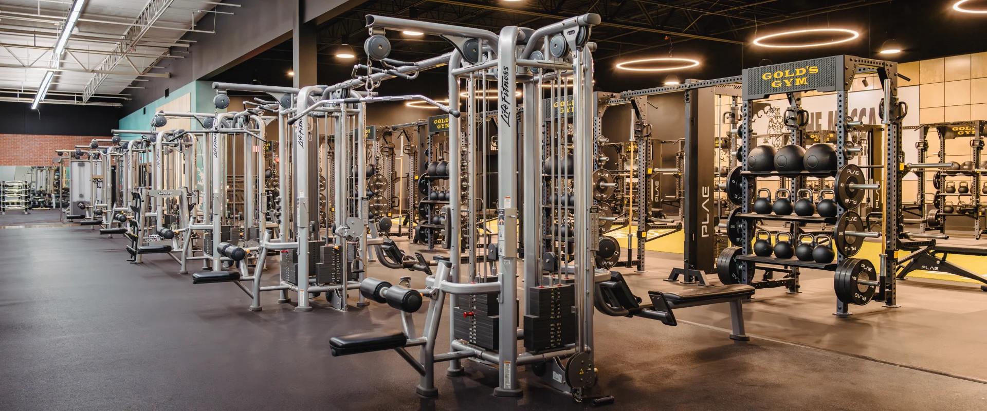 Gold's Gym machine weight area featuring rows of sleek weight training machines, kettlebell racks, and a modern fitness setup under soft, ambient lighting.