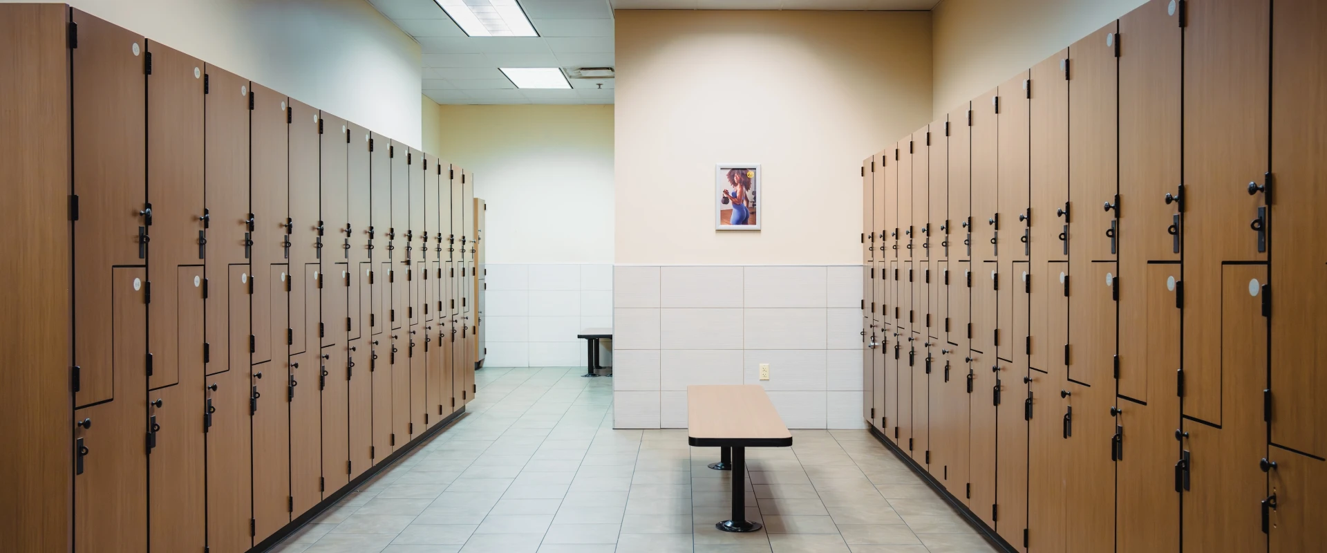 Locker room with wooden lockers lining both sides of the aisle, a bench in the middle. The clean, orderly space conveys a sense of calm and organization.
