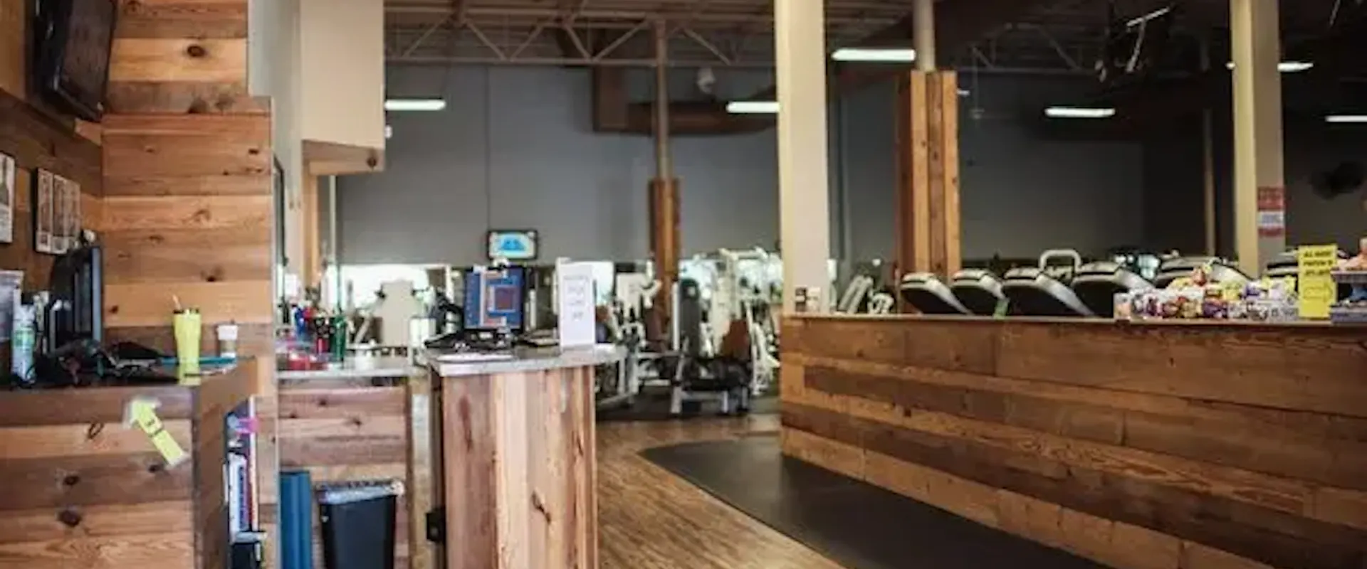 Front desk at Gold’s Gym Goldsboro with wood design and view of cardio and strength equipment behind the counter.
