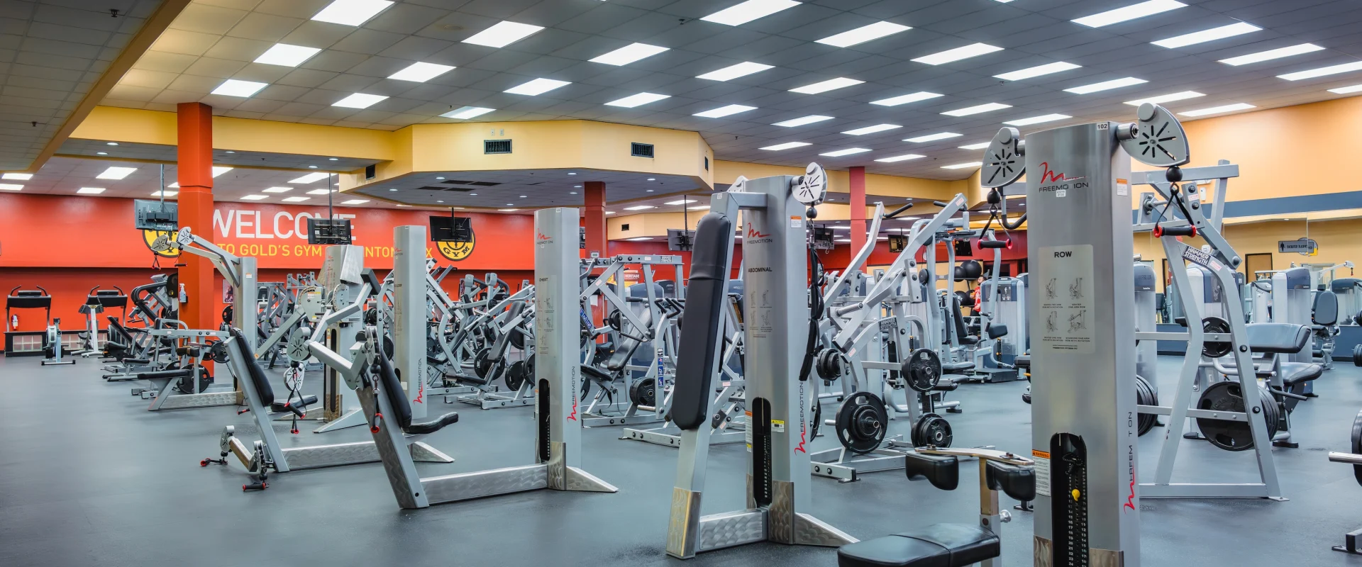 Spacious gym with bright lighting and orange walls, filled with various exercise machines and equipment. A clean, organized, and inviting atmosphere.