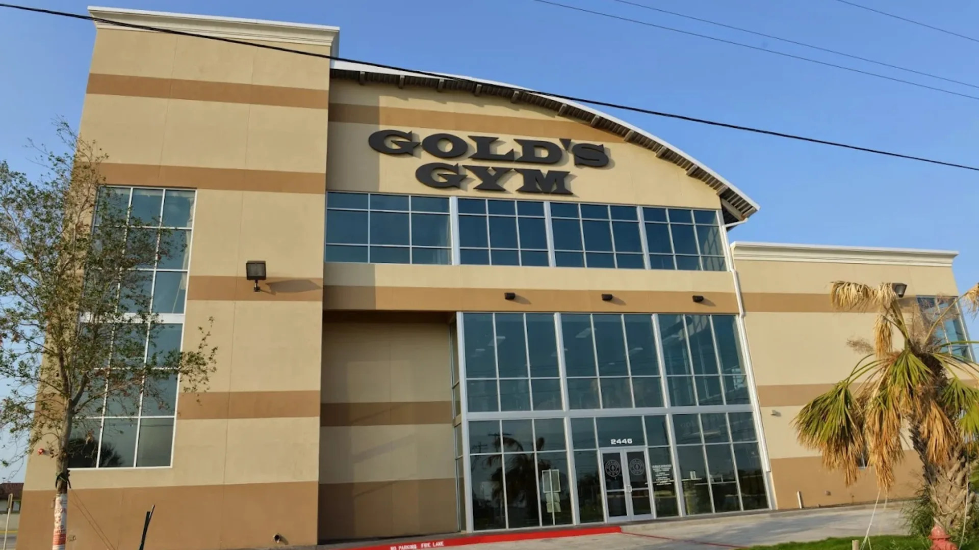 Exterior of Gold’s Gym Laredo North Central with tall windows and tan facade under blue sky.