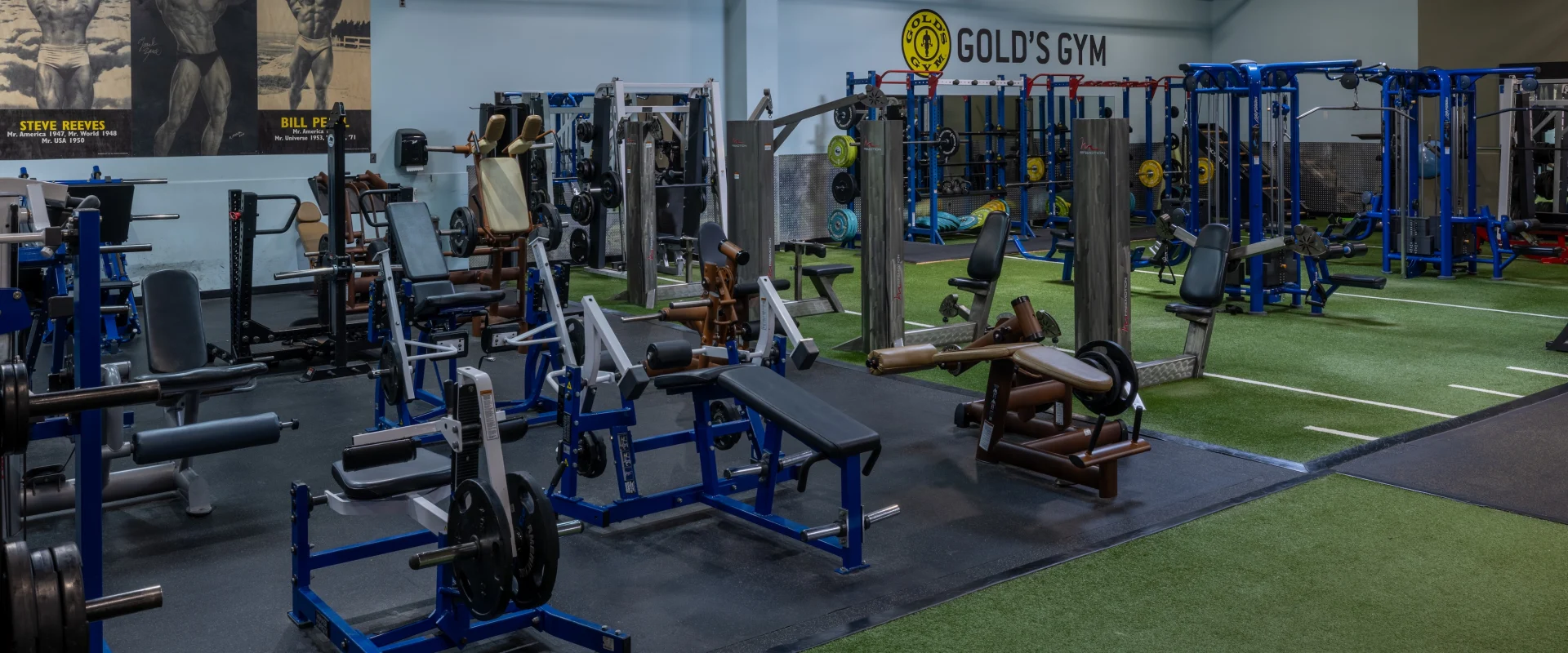 Leg machines, cable machines against pic of body builders on wall