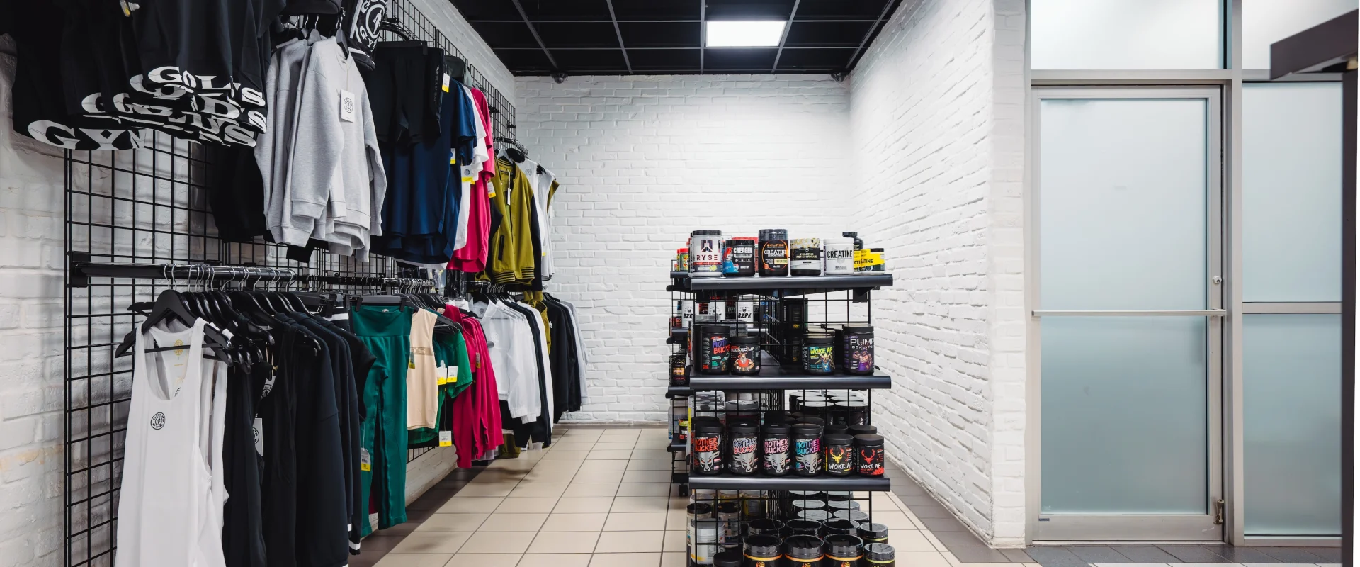 A well-stocked Gold’s Gym Pro Shop showcasing branded apparel, including t-shirts, tank tops, gym shorts, and bags neatly displayed on racks and shelves.