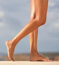 Tanned, slender legs stand on a sandy beach against a backdrop of a cloudy sky.